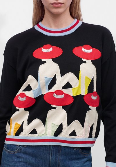 Pull noir avec un design de six femmes stylisées portant des chapeaux rouges à larges bords et des maillots de bain colorés, assises dans différentes poses.