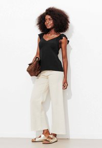 Haut sans manches noir avec bretelles à volants, pantalon beige à jambes larges, et sandales métalliques. Accompagné d'un sac à imprimé léopard.