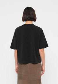 Μαύρο υπερμεγέθες βαμβακερό T-shirt με κοντά μανίκια, στρογγυλή λαιμόκοψη και άνετη εφαρμογή, απεικονίζεται από πίσω πάνω σε απλό φόντο.