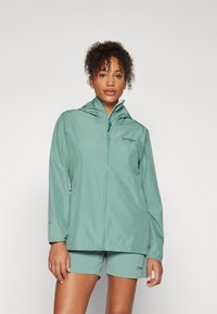 Giacca impermeabile leggera di colore verde menta con chiusura lampo, cappuccio e polsini elasticizzati, abbinata a pantaloni corti coordinati.