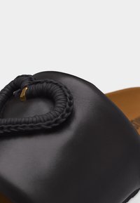 Μύτη μαύρου δερμάτινου παπουτσιού με πλεχτή λεπτομέρεια βρόχου στερεωμένη με ένα μικρό χρυσό μεταλλικό κομμάτι.