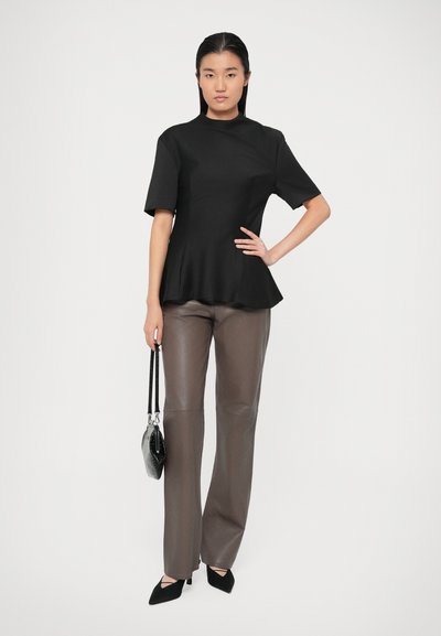 Top negru cu mânecă scurtă, cu tiv peplum, asortat cu pantaloni gri lucioși. Modelul ține o geantă mică neagră și poartă pantofi cu vârf ascuțit negri.