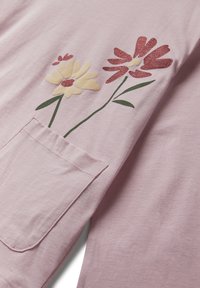 Camisa de manga larga rosa claro con diseño floral que presenta flores brillantes en amarillo y rojo, y un bolsillo lateral. Textura de tejido suave y liso.