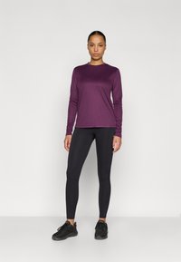 Pitkähihainen violetti paita, mustat leggingsit ja mustat urheilukengät. Sileä kangas, istuva muotoilu, yksinkertainen pääntie ja saumaton viimeistely.