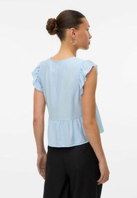 Lyseblå bluse med korte ærmer og flæseærmer samt peplum-design. Teksturstof med en glat overflade, kombineret med sorte bukser.