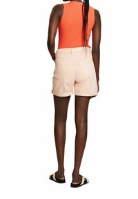 Pantalones cortos de mezclilla rosa con dobladillos enrollados, bolsillos traseros, combinados con una camiseta de tirantes de canalé naranja. Diseño sencillo, ideal para el uso diario en clima cálido.