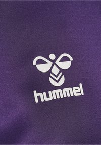 Logo stylisé d'abeille blanche et texte "hummel" imprimés sur un fond de tissu texturé violet.