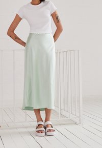 Maglietta bianca a maniche corte con bordi ondulati, abbinata a una gonna midi in satin verde menta e sandali bianchi chunky con design a strisce.