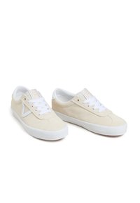 Beige suede sneakers featuring white laces and rubber soles, with a textured upper and circular logo detail on the tongue.