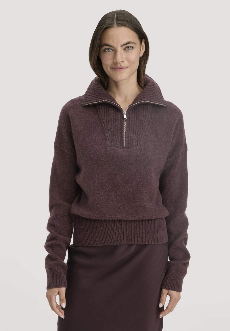 Bordeaux trui met hoge kraag, halve rits aan de voorkant, geribbelde textuur en een strakke pasvorm. Gecombineerd met een bijpassende strakke rok.