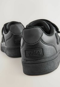 Baskets en cuir noir avec une finition texturée, dotées d'une sangle, d'un col rembourré et d'un logo Pokémon sur le côté. Design de talon arrondi.