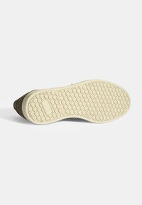 Die Schuhsohle weist ein strukturiertes, gemustertes Gummi in hellbeige auf, mit einem oberen Teil aus braunem Wildleder, das durch eine umrandete Naht charakterisiert ist.