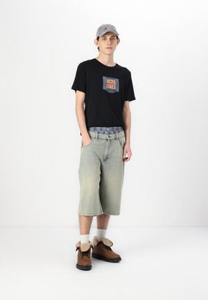 Must mustaga mustri oranzh logo, heled sinised laiad lühikesed püksid ja pruunid saapad, millel on fleece vooder. Hall müts ja valged sokid täiustavad välimust.