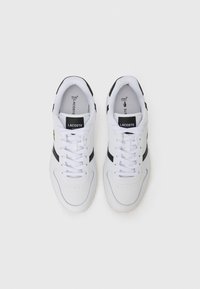 White athletic sneakers with black accents, leather upper, lace-up design, perforated toe, and branded tongue featuring green logo.