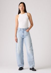 Top bianco senza maniche a coste abbinato a jeans a gamba larga di colore azzurro chiaro, con tasche laterali e vestibilità comoda. Scarpe nere completano l'outfit.