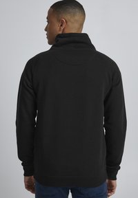 Maglione nero a pullover con colletto alto, polsini rigati e una texture liscia. Caratterizzato da un design a manica raglan e uno stile minimalista.