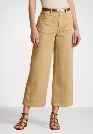 Khaki wide-leg trousers made of cotton, featuring two front pockets and a visible button closure. Paired with brown strappy sandals.