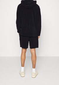 Sweat à capuche en polaire bleu marine avec une poche kangourou, assorti à un short coordonné. La tenue présente une texture douce et une coupe décontractée.