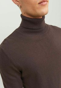 Maglione a collo alto marrone realizzato in un tessuto morbido e testurizzato. Presenta un collo alto e una silhouette aderente. Design minimalista senza motivi o dettagli.