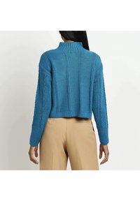 Maglione azzurro a maglia corto con collo alto, texture a coste e motivi a treccia laterali, abbinato a pantaloni beige.