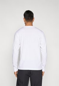 Λευκό μακρυμάνικο μπλουζάκι με στρογγυλή λαιμόκοψη, κατασκευασμένο από βαμβακερό μείγμα, με απλό σχέδιο και εφαρμοστά μανίκια. Η πίσω όψη δείχνει λεία υφή.