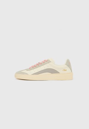 Tenisica u krem i svijetlosivoj brušenoj koži, s ružičastim vezicama, perforiranim detaljima i bež gumeni potplat. Zlatni detalj nosi oznaku „1964.”