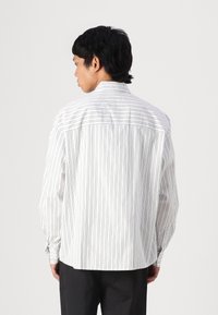 Gestreiftes Hemd in Weiß und hellen Farben, mit Button-Down-Kragen und langen Ärmeln. Gerader Saum mit einer einzelnen Yoke-Seam-Detail auf der Rückseite.