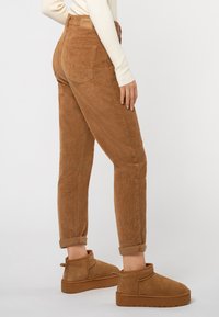 Braune Cordhosen mit taillierter Form, umgeschlagenen Säumen und Gesäßtaschen, kombiniert mit passenden braunen Ankle-Boots aus Wildleder.