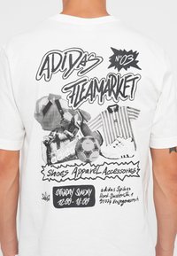 Biela tričko s čiernym grafickým dizajnom, na ktorom je text "Adidas Fleamarket", obrázky športových predmetov a podrobnosti o udalosti.