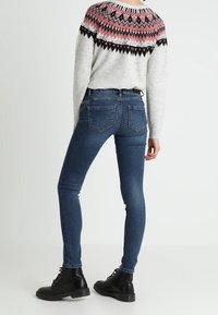 Neulottu pusero, jossa vaaleanpunainen ja musta kuvio yläosassa, yhdistetty tummansinisiin kapealahkeisiin farkkuihin ja mustiin nauhallisiin nilkkureihin.