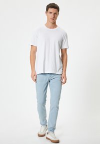 Camiseta de algodón blanca y jeans de color azul claro combinados con zapatillas blancas con suelas marrones. Diseño sencillo con un ajuste holgado.