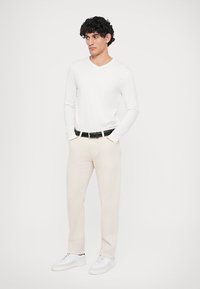 Camicia bianca a maniche lunghe con scollo a V abbinata a pantaloni beige. Cintura nera con fibbia in metallo, sneakers bianche. Texture lisce, design semplice.