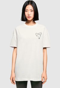Hvid oversized t-shirt lavet af bomuld, med en sort grafik af to hjerteformede balloner på venstre brystområde. Korte ærmer.