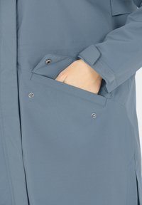 Ljusblå jacka med framficka, knappstängning och texturerat tyg. Har en enkel design och justerbara manschetter.