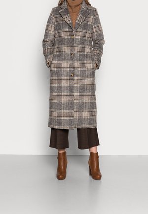 Rutig ullkappa i grått, beige och brunt, med snedskuren krage, knappstängning och sidofickor, kombinerad med bruna klackstövlar.