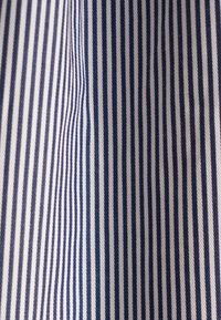 Tissu à rayures verticales bleu et blanc avec un léger pli créant une variation dans l'espacement et la direction des rayures.