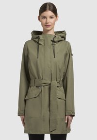 Olijfgroene waterdichte jas met een trekkoordcapuchon, een riem in de taille, twee voorzakken en een drukknoopsluiting. Glad, lichtgewicht stof.