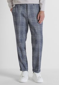 Grau karierte Hose mit entspannter Passform, featuring ein kariertes Muster und seitlichen Taschen, kombiniert mit weißen Sneakern.