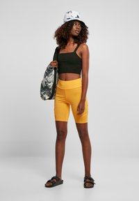 Zwarte cropped top, gele fietsbroek, gestippelde tas, witte tie-dye bucket hat en zwarte sandalen. Eenvoudig ontwerp met functionele details.