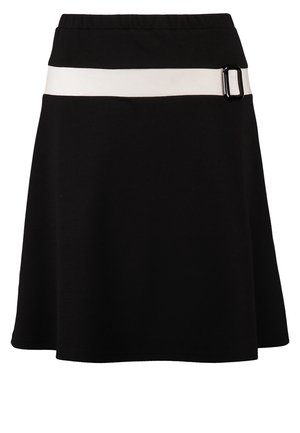 Vrouw draagt een witte top met zwarte rand, zwarte rok met witte riem, zwarte panty's, zwarte hakken, houdt een witte handtas vast.