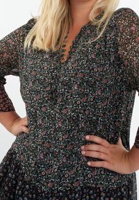 Vestido de manga larga en tejido negro transparente con estampado floral en tonos verdes, rojos y púrpuras. Presenta un escote con forma de ola y un cuerpo texturizado.