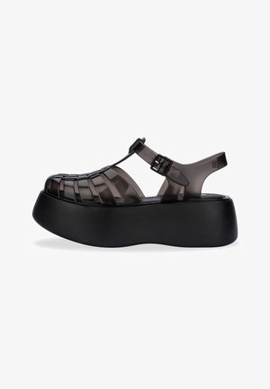 Czarne sandały na platformie z przezroczystym, plecionym wierzchem, regulowaną klamrą i teksturowaną czarną podeszwą.