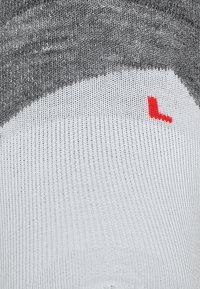 Grå og hvid strikket sok med et ribbet mønster og et lille rødt "L" på fodsålen. Materialerne er bløde og elastiske, designet til komfort.