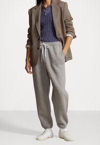 Grå mjukisbyxor med elastisk midja och dragsko, kombinerade med en lila kabelstickad polotröja och en brun hundtandsmönstrad kavaj. Vita sneakers.