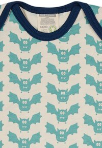 Bio-Baumwoll-Overall mit cremefarbenem Hintergrund, der ein sich wiederholendes Muster von teal-farbenen Cartoon-Fledermäusen zeigt. Marineblauer Besatz am Hals.