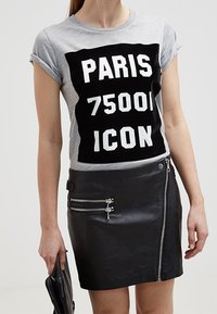 Graues Baumwoll-T-Shirt mit schwarzem Grafikdruck "PARIS 75001 ICON." Kombiniert mit einem eng anliegenden schwarzen Leder-Minirock mit Reißverschlusstaschen.