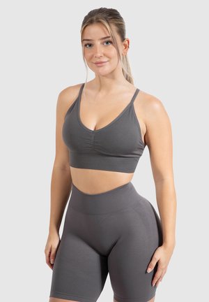 Grijze sport-beha en high-waisted shorts gemaakt van gladde, rekbare stof. De beha heeft een V-hals design met geplooide stiksel voor textuur.