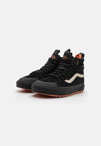 Høye svarte sneakers med suede-overdel, beige detaljer, gummitåhette og teksturert oransje yttersåle. Snøring med trekkfliker.