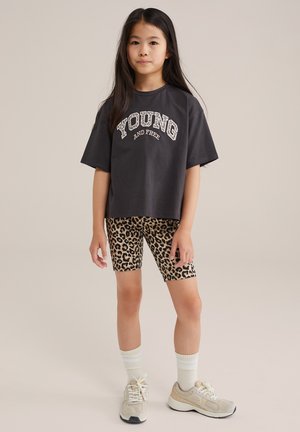 Czarny t-shirt w kolorze ciemnoszarym z białym napisem "YOUNG AND FREE", w połączeniu z szortami rowerowymi w tygrysie plamy. Lekka tkanina, luźny krój i okrągły dekolt.