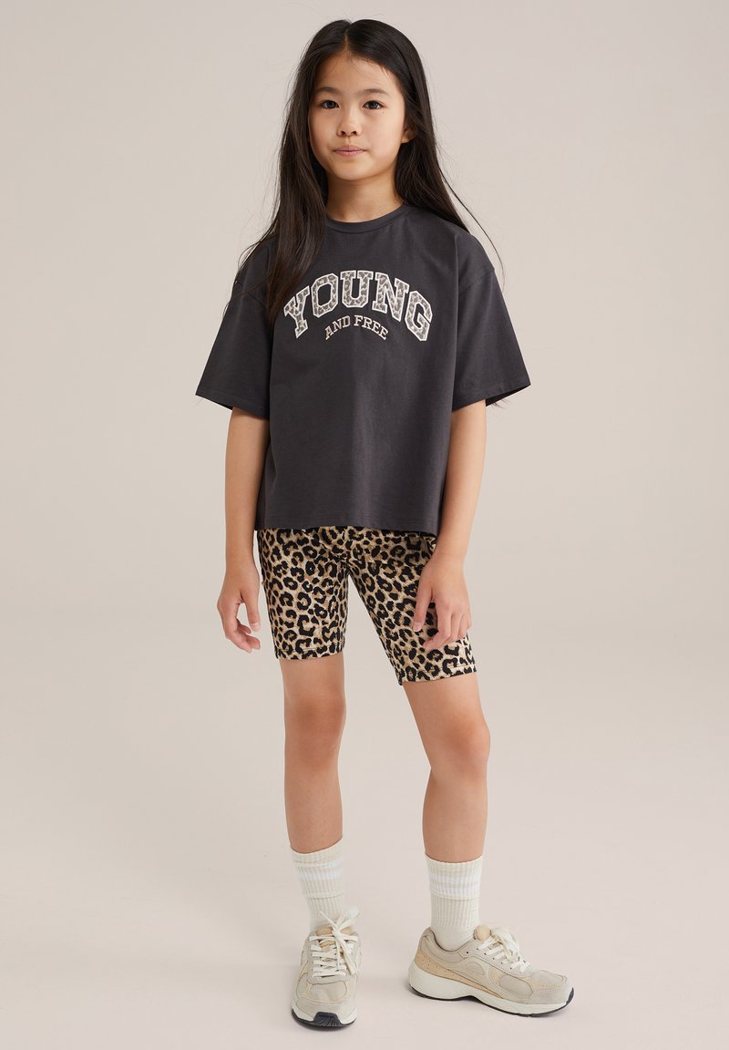 Mörkgrå t-shirt med vit text "YOUNG AND FREE", i kombination med cykelshorts i leopardprint. Lättviktig material, avslappnad passform och rundad halsringning.